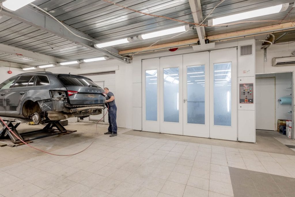 Work Mechanic repairing a car indoors at an auto workshop, focusing on vehicle maintenance.