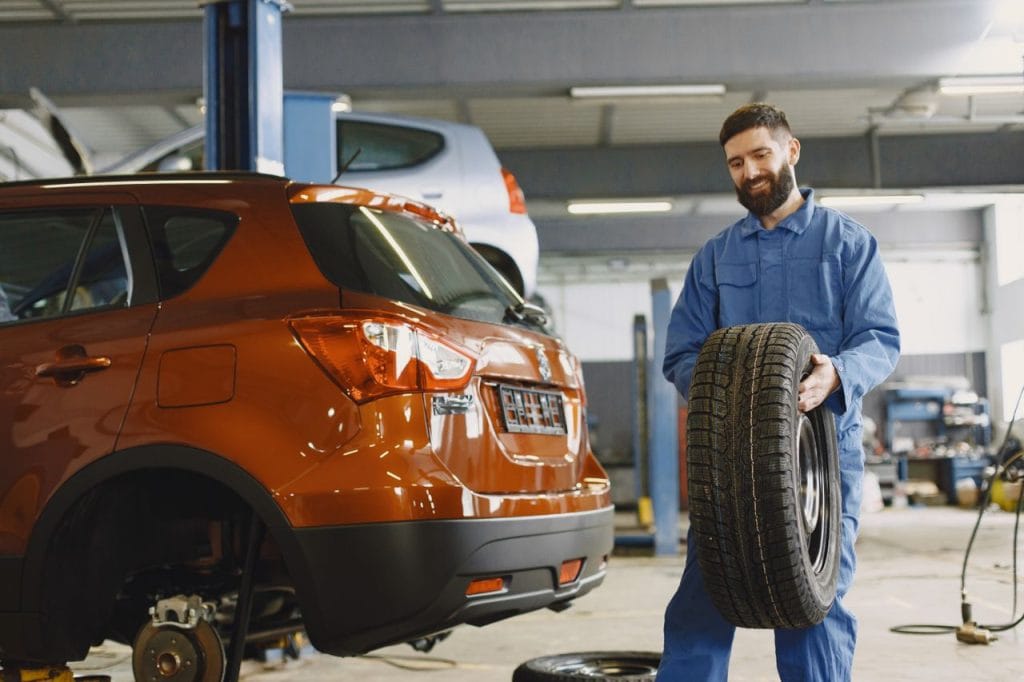 Work Mechanic holding a tire in a vehicle repair shop, showcasing automotive maintenance.