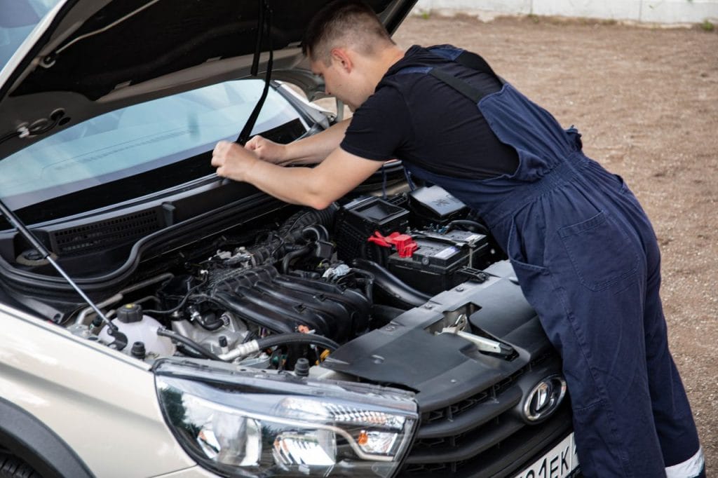 Work Mechanic working on a car engine with hood open, showcasing automotive repair skills.