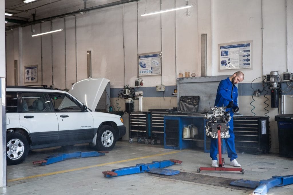 Work Mechanic in blue coveralls working on an engine in a modern auto repair workshop.