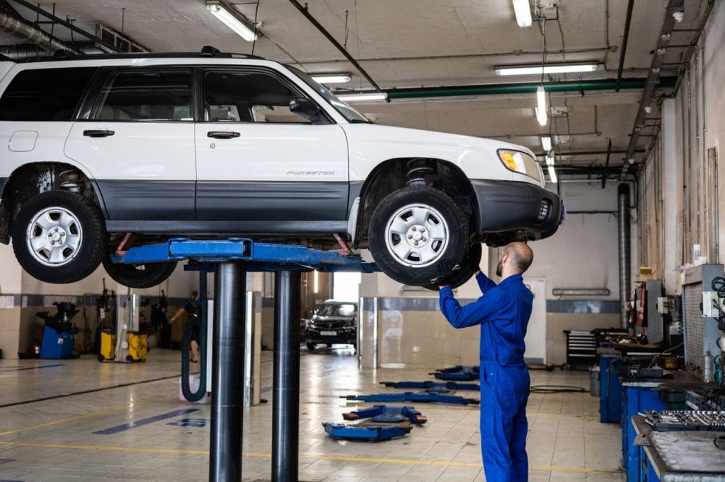 Work A mechanic inspecting a white SUV lifted in a well-lit auto repair shop.