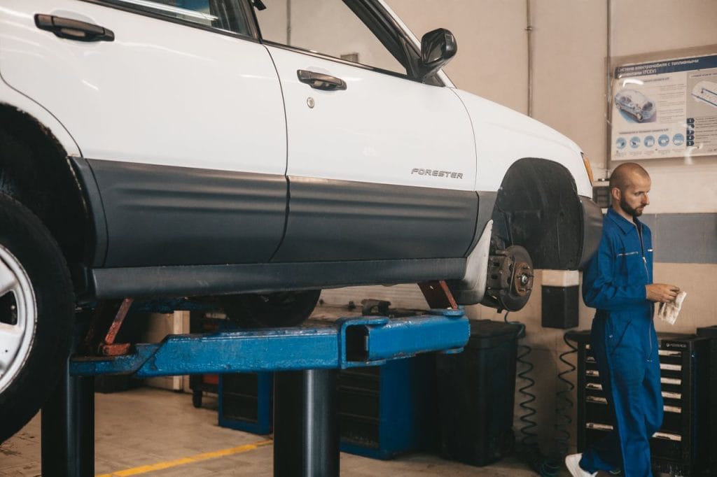 Work Mechanic evaluating a car on a lift for maintenance in an auto workshop.